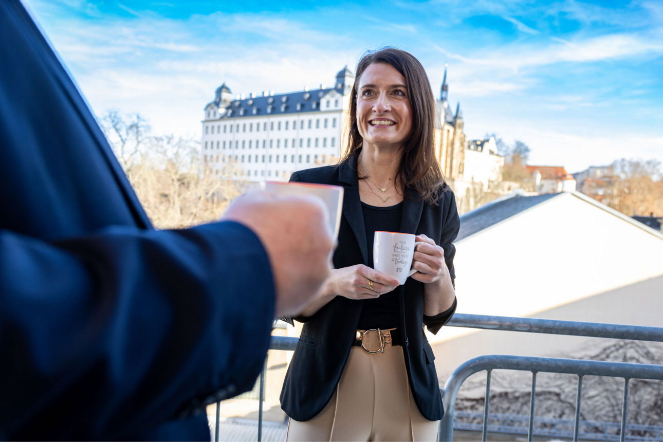 Zwei Personen stehen mit Kaffeetassen in der Hand auf einem Balkon