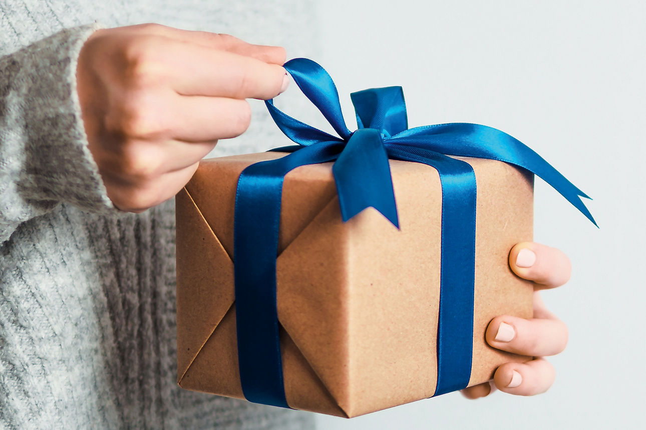 Eine Person hält ein Geschenk mit blauer Schleife in den Händen