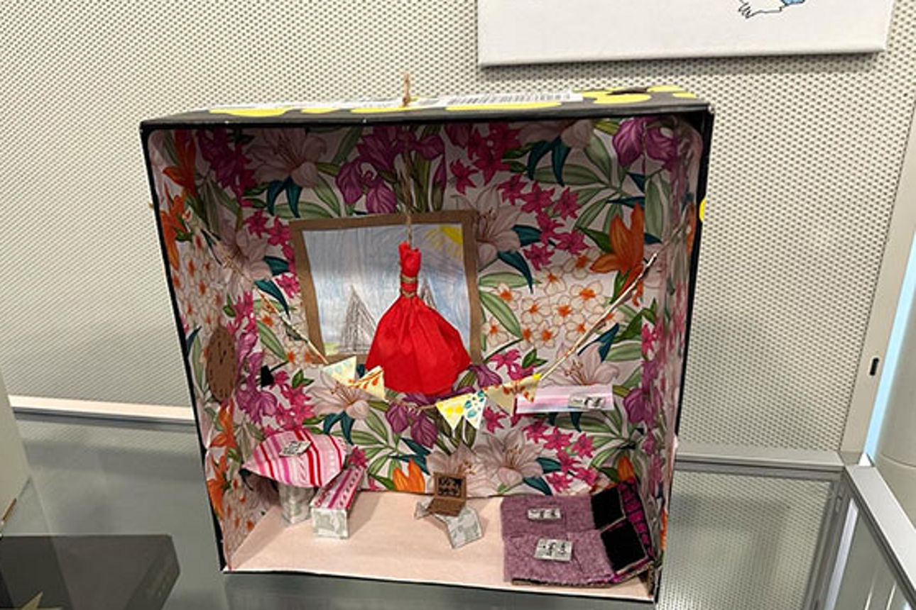 Ein Kunstprojekt eines Kindes, das ein Puppenzimmer mit bunten Blumenwänden aus einem Schuhkarton darstellt