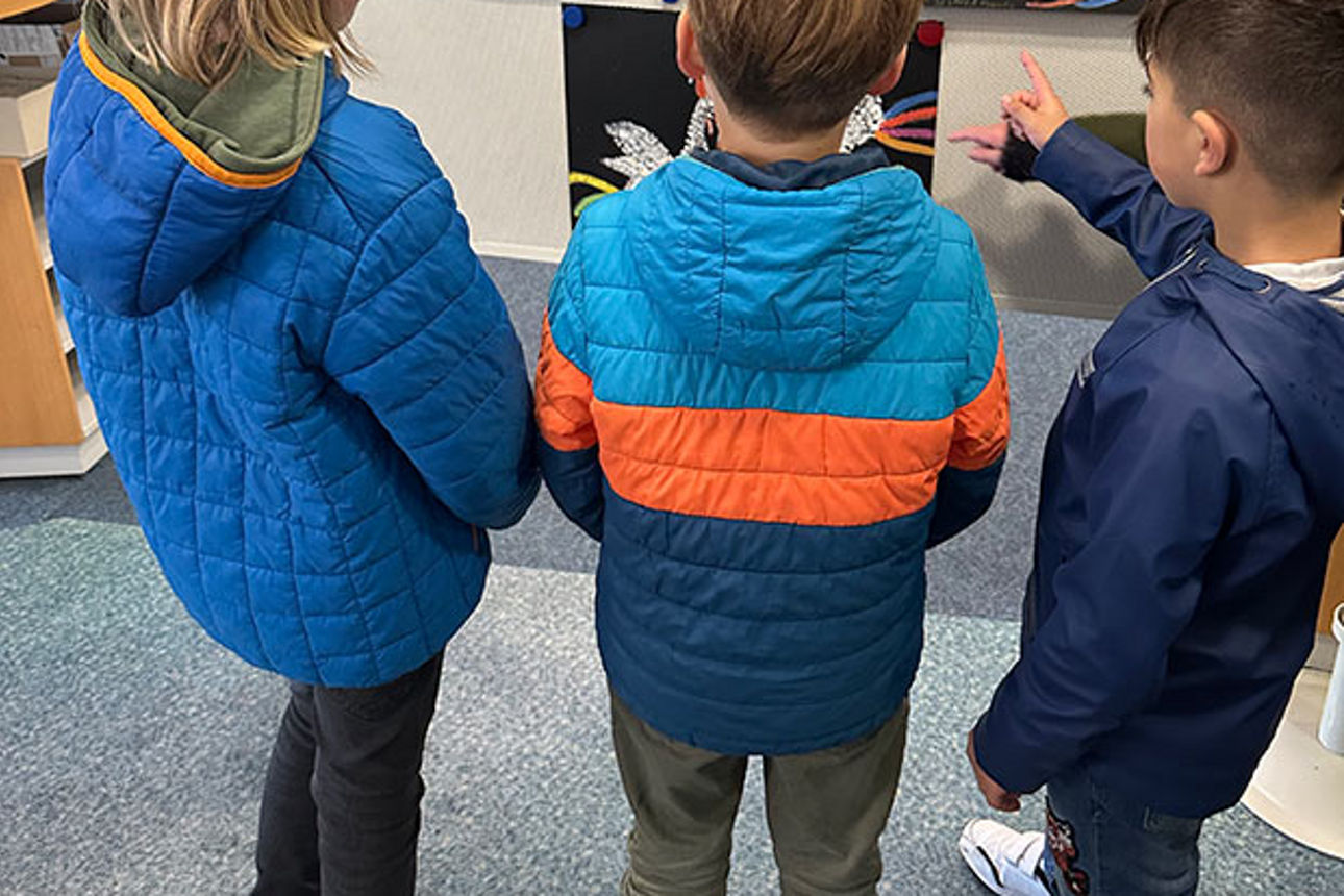 Drei kleine Kinder bewundern eine Reihe von Gemälden mit streitenden Hähnen