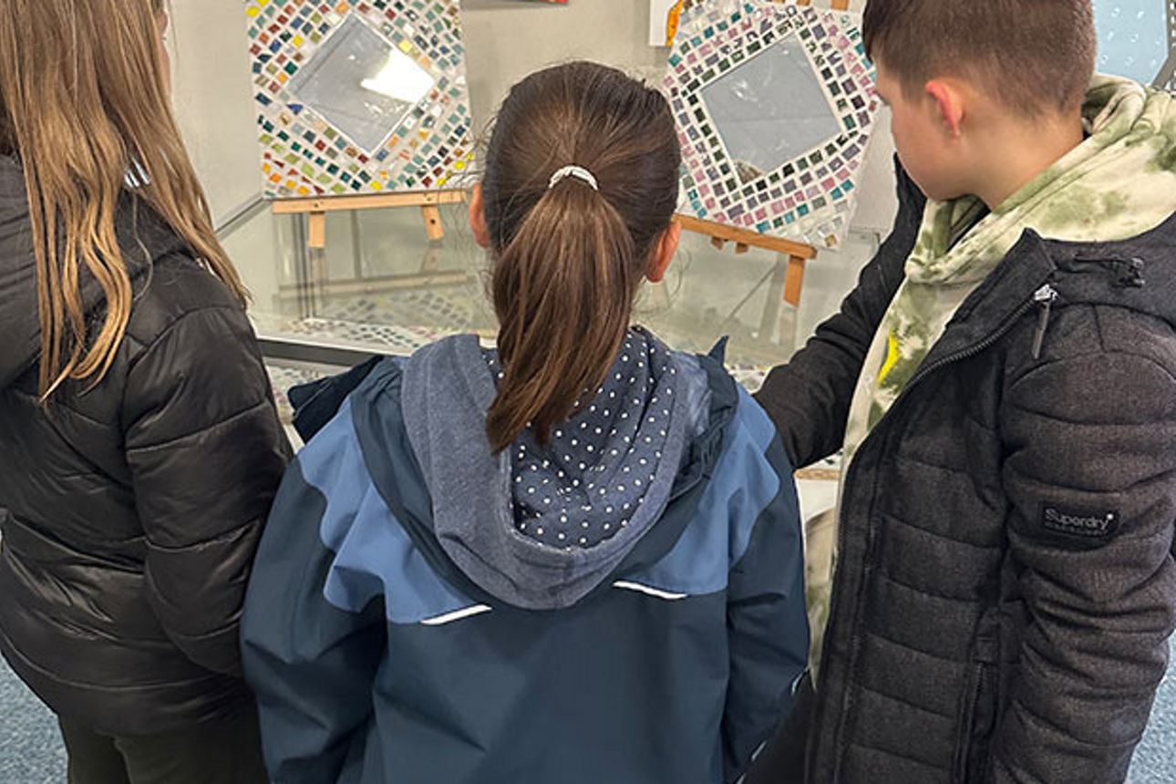 Drei Kinder bewundern eine Reihe von Kunstobjekten wie Zeichnungen, handgefertigtes Spielzeug und verzierte Spiegel