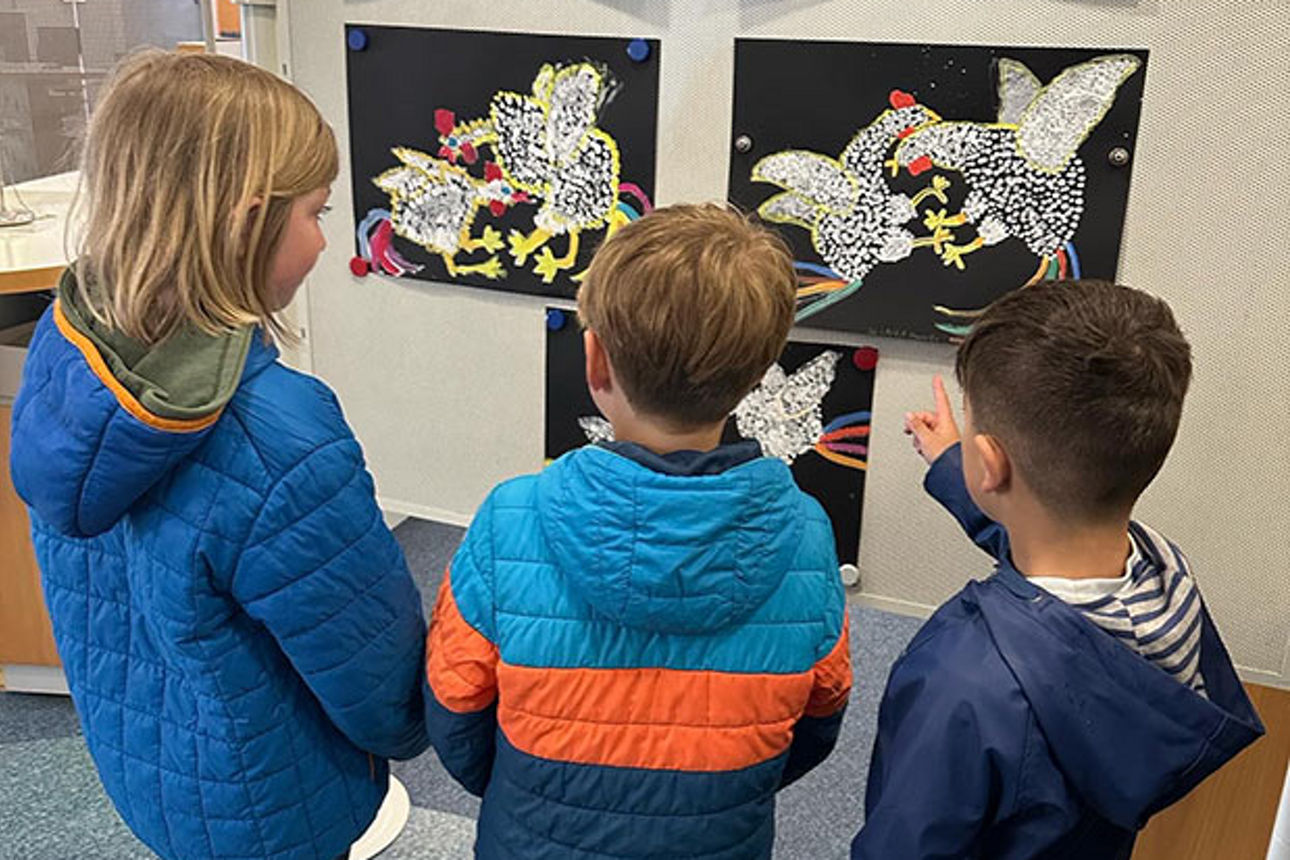 Drei kleine Kinder bewundern eine Reihe von Gemälden mit streitenden Hähnen