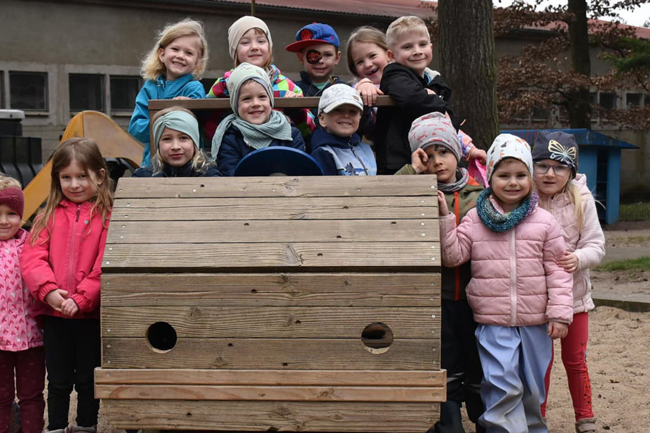 Betreute Kinder der ASB-Kita Sonnenkäfer sitzen auf der Holzeisenbahn und lächeln