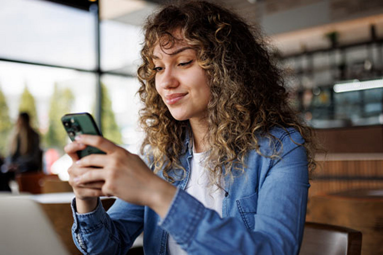 Junge Frau sitzt in einem Cafe und liest etwas auf ihrem Spartphone