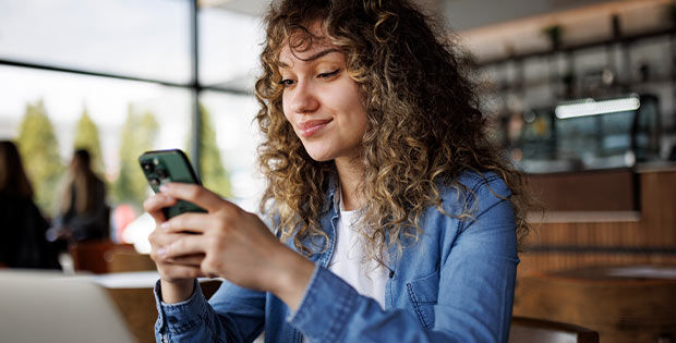 Junge Frau sitzt im Cafe und liest auf ihrem Smartphone
