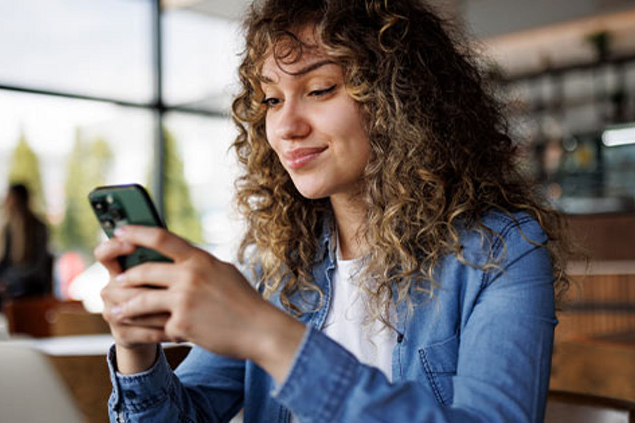 Junge Frau sitzt im Cafe und liest auf ihrem Smartphone