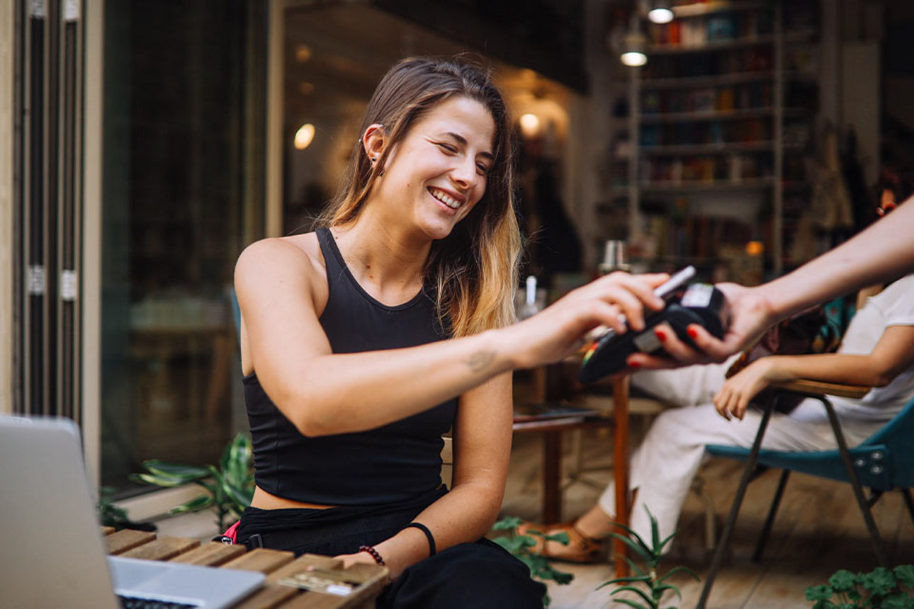 Junge Frau bezahlt auf der Terrasse eines Cafés mit dem Smartphone.