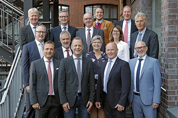 Eine Gruppe von 13 Personen, die in einem formellen Rahmen zusammenstehen