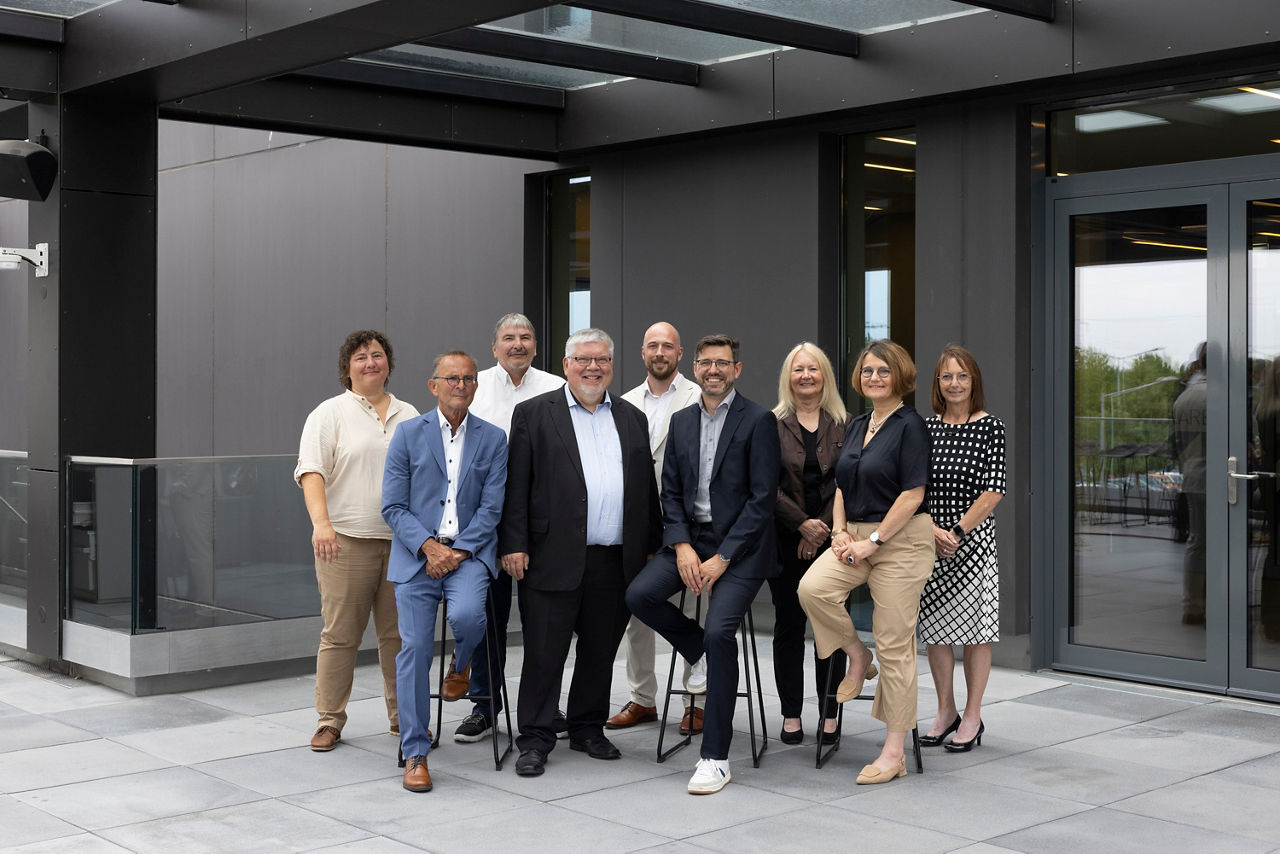 Auf dem Bild sitzen neun Personen für ein Gruppenfoto zusammen, vier Frauen und fünf Männer. Sie blicken freundlich in die Kamera.