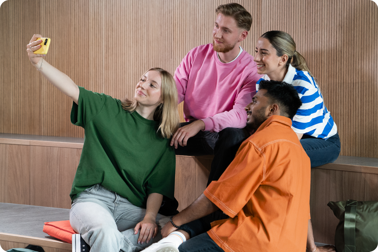 Eine Gruppe aus vier Jugendlichen lächelt in eine Smartphonkamera für ein Selfie