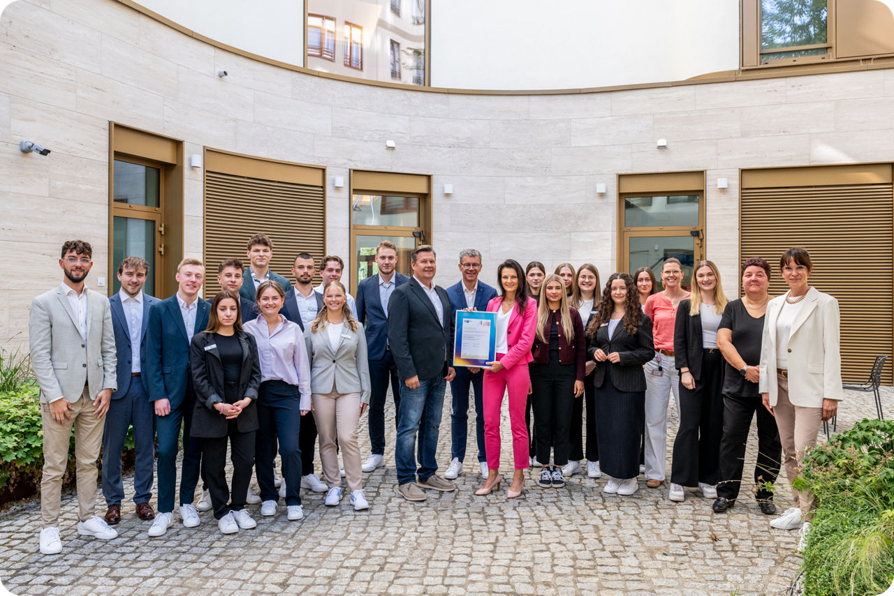 Eine Gruppe von Auszubildenden stehen im Halbkreis für ein Gruppenfoto im Innenhof der Zentrale der Berliner Volksbank und schauen in die Kamera
