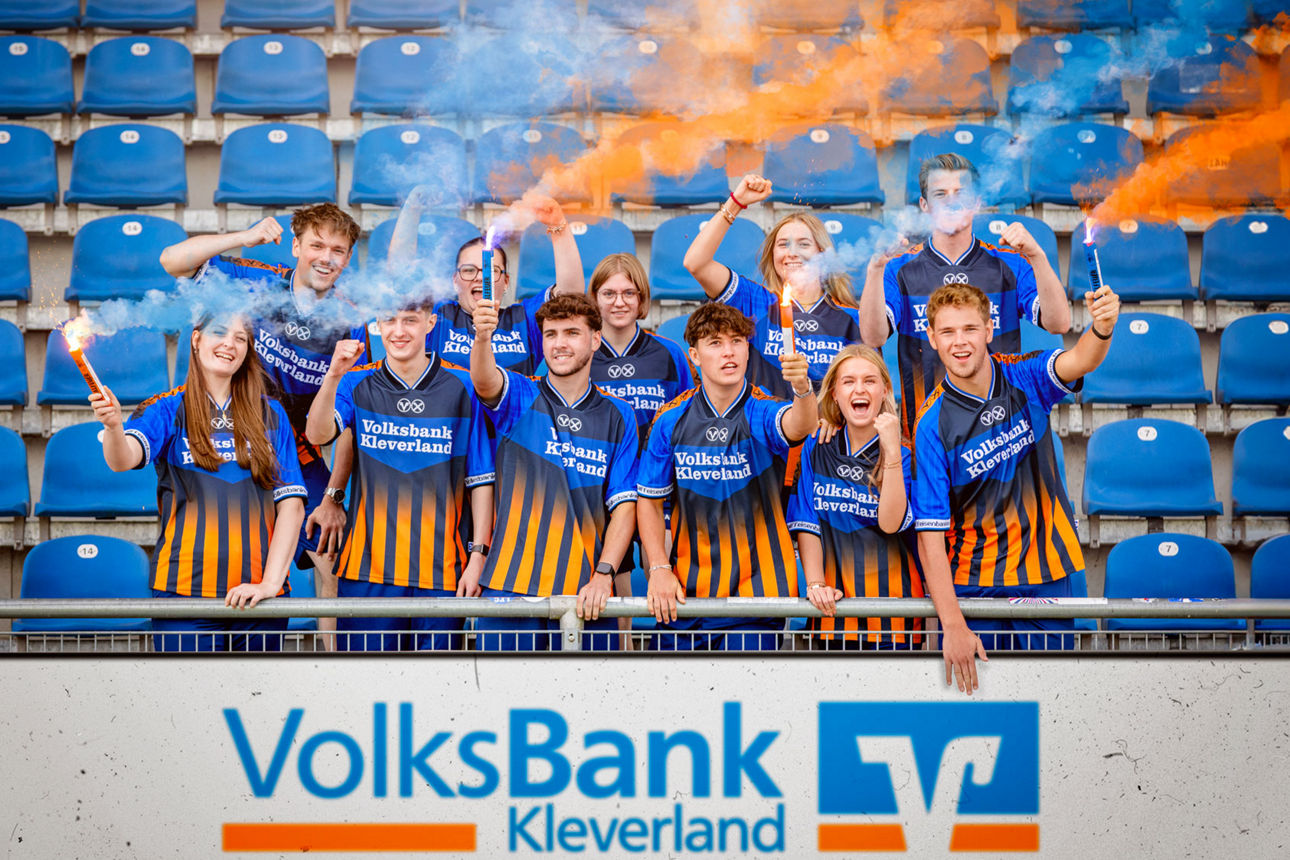 Gruppenfoto Auszubildende auf Tribüne im Fussballstadion mit blauen und orangenen Bengalos in der Hand