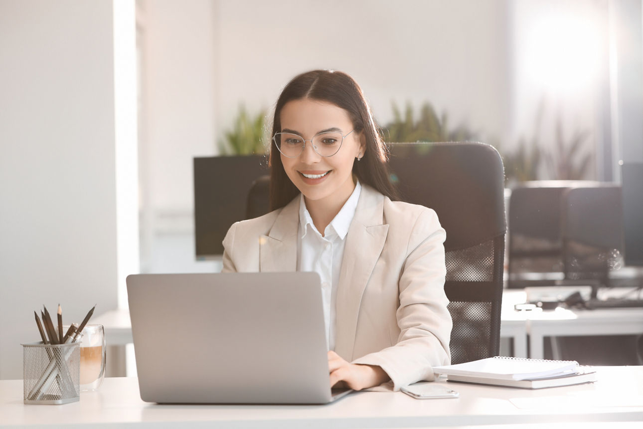Junge Frau sitzend am Schreibtisch und schaut auf den Laptop