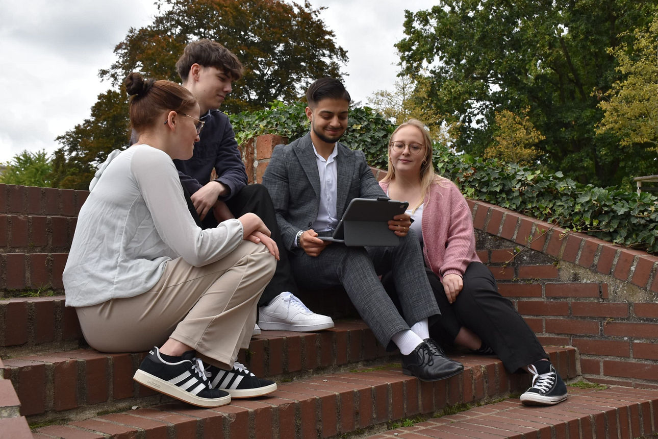 Auszubildende sitzen auf einer Treppe und schauen gemeinsam auf ein Tablet