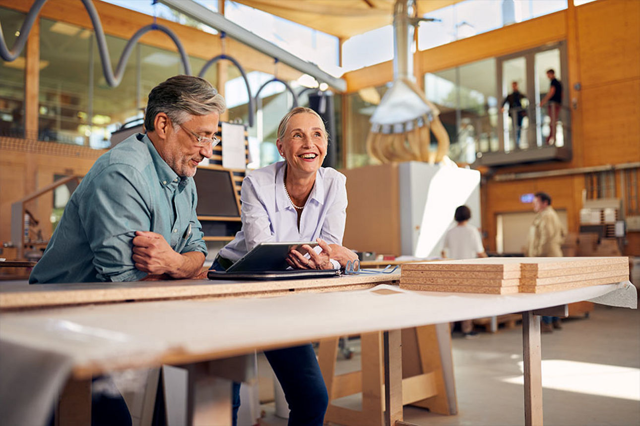 Zwei Personen, die über einen Tisch gebäugt an einem Tablet arbeiten