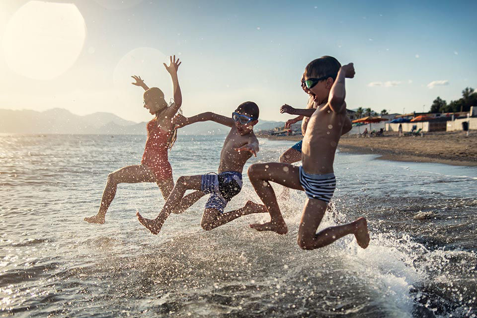 drei Kinder am Strand springen ins Wasser