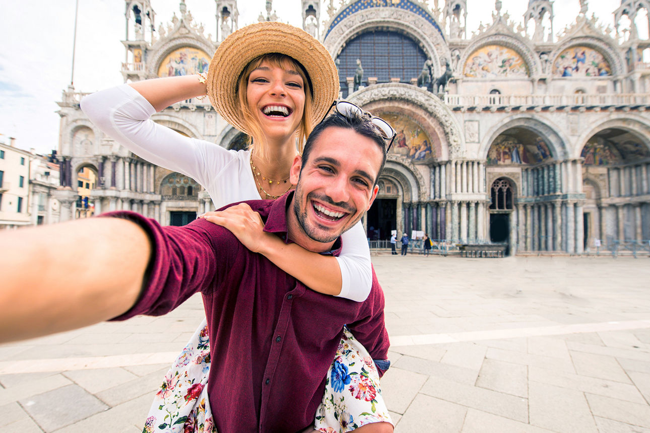  Ein Mann trägt eine Frau mit Strohhut auf einem Platz in Venedig