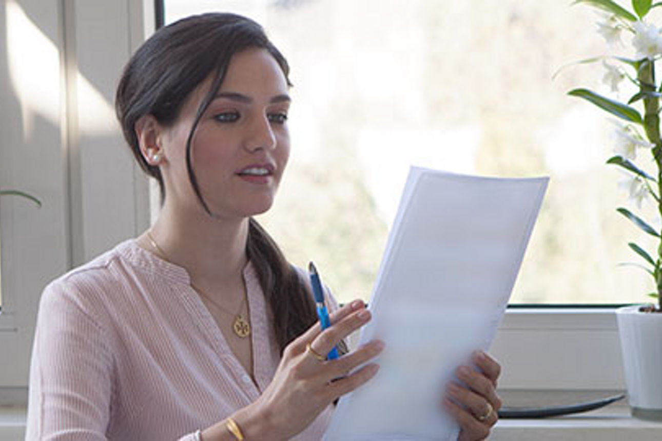 Eine junge Frau sitzt am Fenster und sieht sich ein Dokument an
