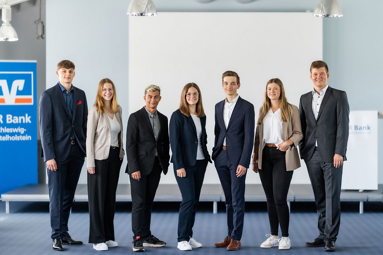 Drei junge Frauen und vier junge Männer vor einer Bühne