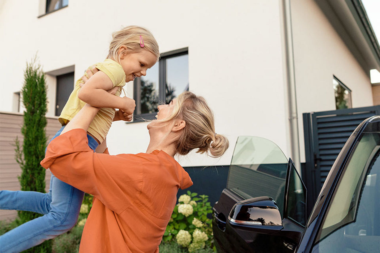 Junge Frau in einem Vorgarten hebt ein Kind in die Luft