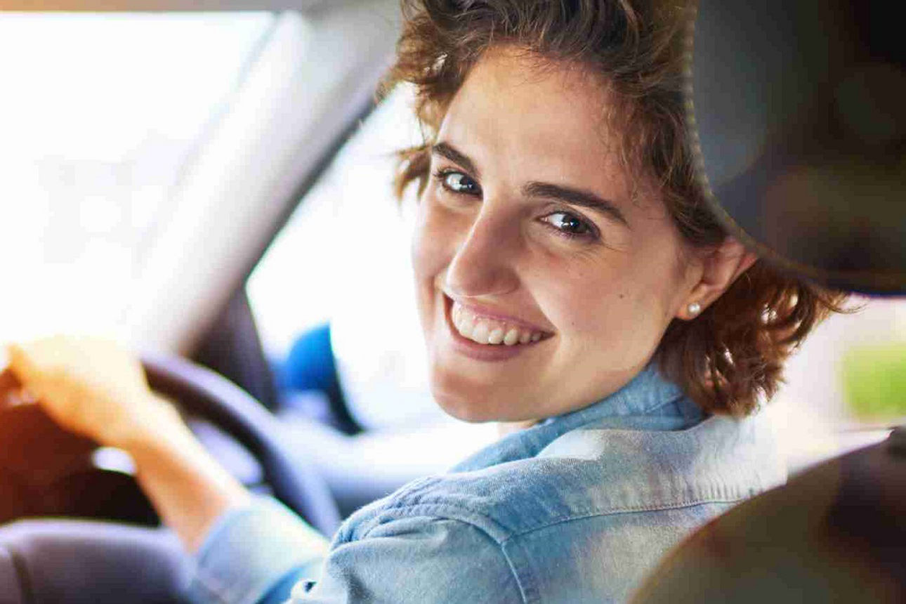 Eine lächelnde Frau im Auto schaut über ihre linke Schulter zurück 