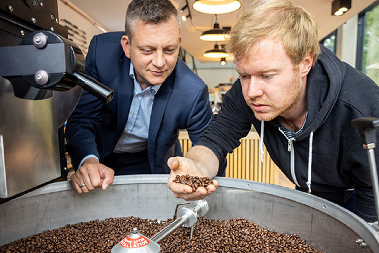 Zwei Männer schauen sich geröstete Kaffeebohnen an Zwei Männer schauen sich geröstete Kaffeebohnen an