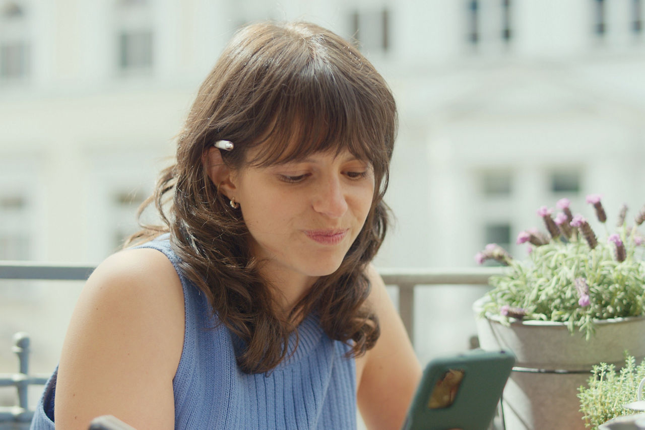 Eine junge Frau sitzt auf dem Balkon und schaut auf ihr Handy. 