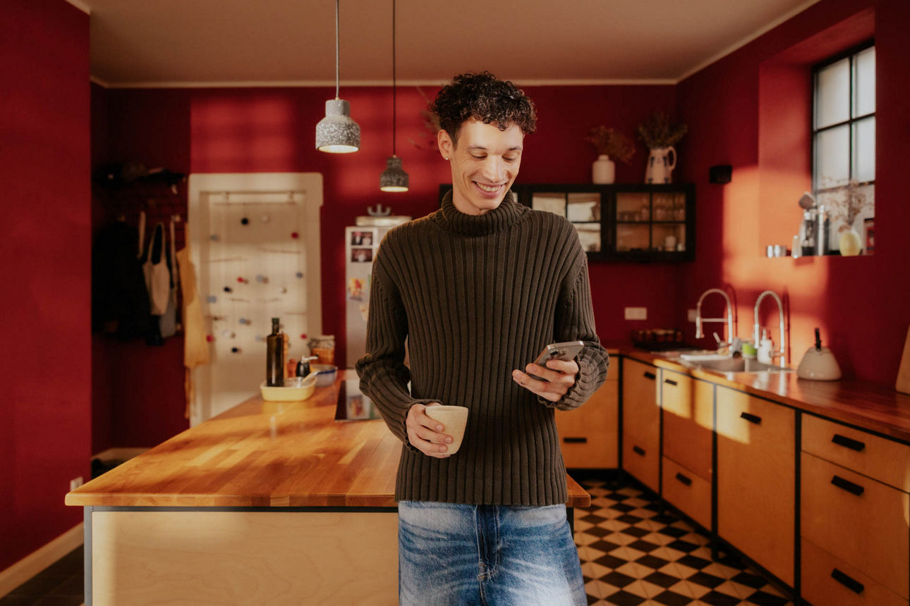 Junger Mann in der Küche mit dem Smartphone in der Hand
