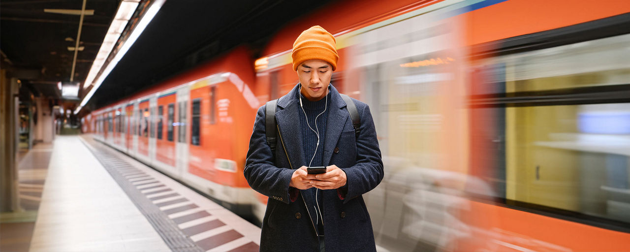 Mann in einer U-Bahn-Station, der auf sein Smartphone schaut