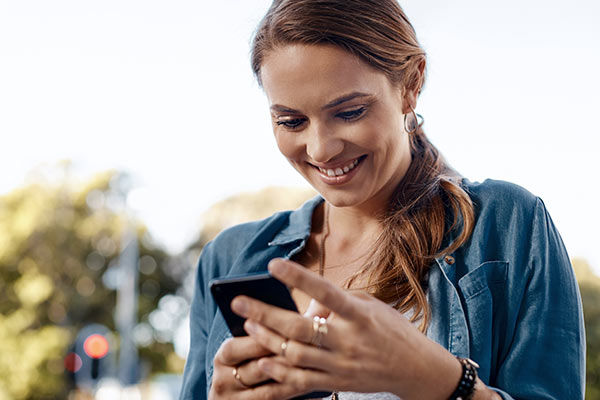 Junge Frau schaut lächelnd auf ihr Smartphone