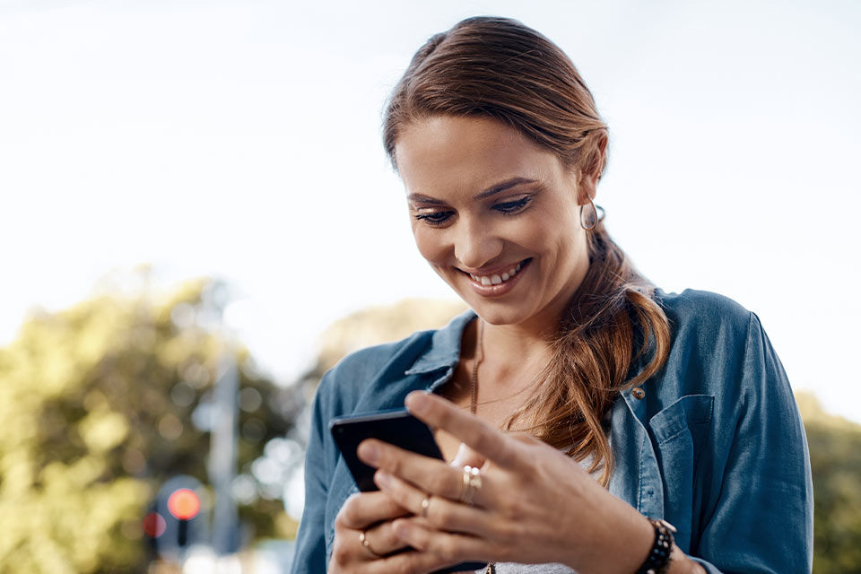Junge Frau schaut lächelnd auf ihr Smartphone