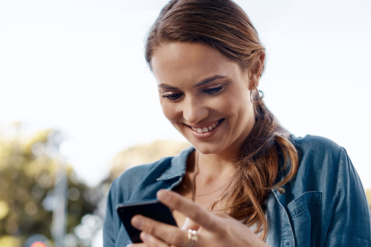 Junge Frau schaut lächelnd auf ihr Smartphone
