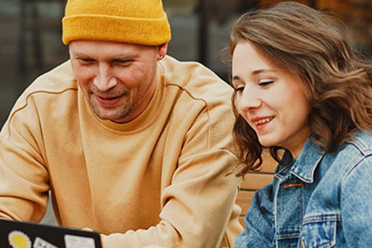 Ein Mann und eine Frau sitzen auf einer Bank, konzentrieren sich auf einen Laptop und führen eine gemeinsame Diskussion im Fr