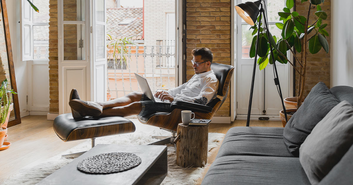 Mann sitzt im Sessel und hat sein Laptop vor sich auf den Beinen liegen.