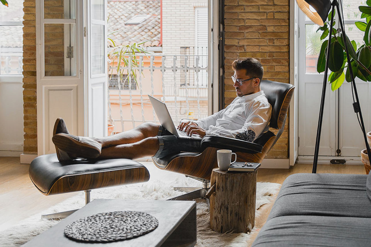 Mann sitzt im Sessel und hat sein Laptop vor sich auf den Beinen liegen.