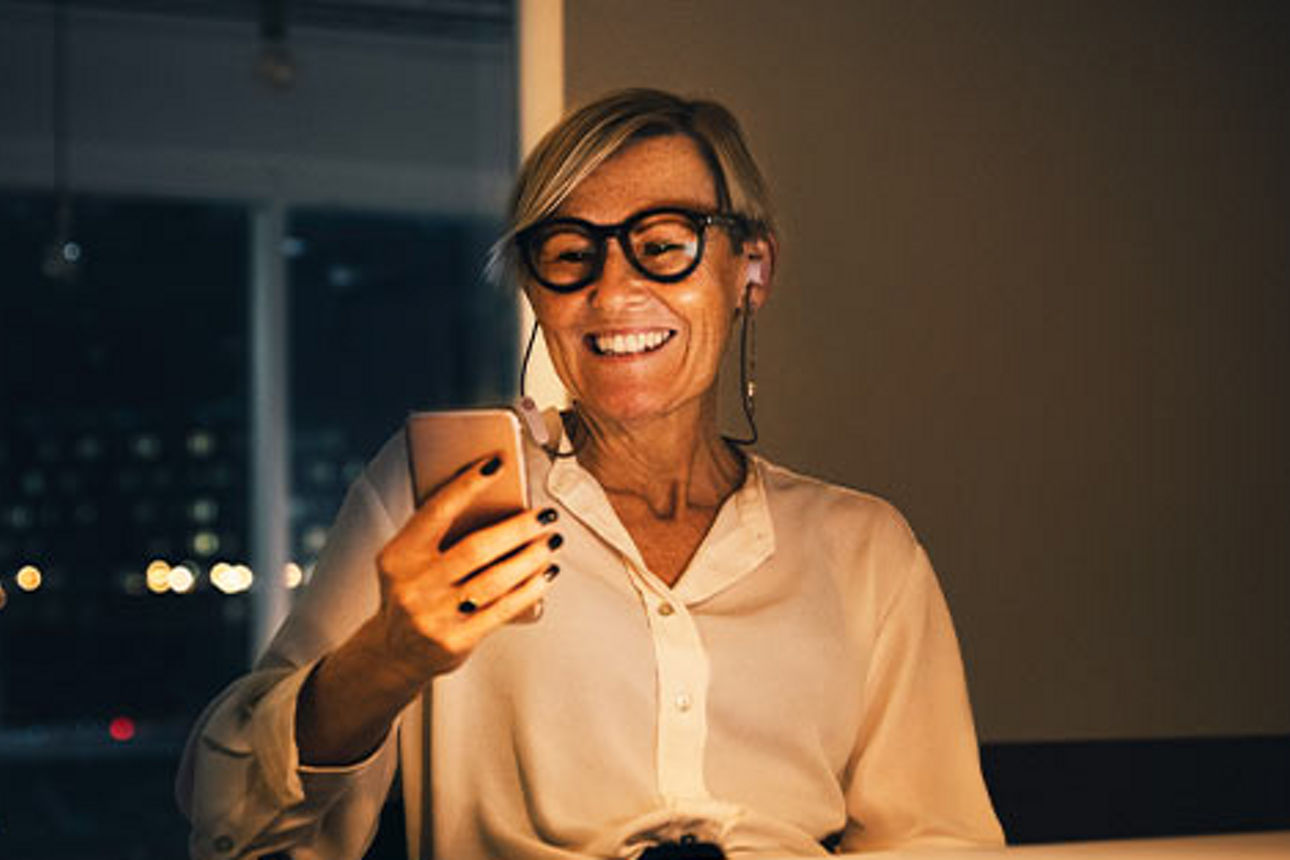 Eine Geschäftsfrau schaut lächelnd auf ihr Smartphone