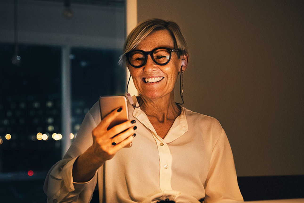 Eine Geschäftsfrau schaut lächelnd auf ihr Smartphone