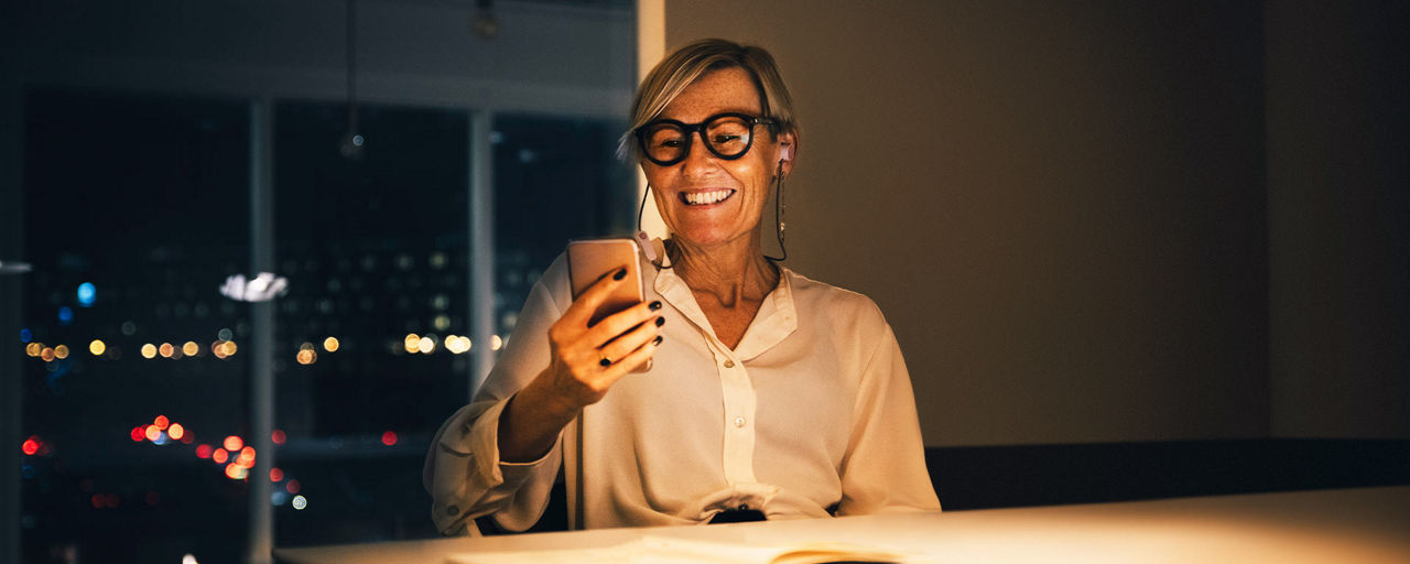 Eine Geschäftsfrau schaut lächelnd auf ihr Smartphone