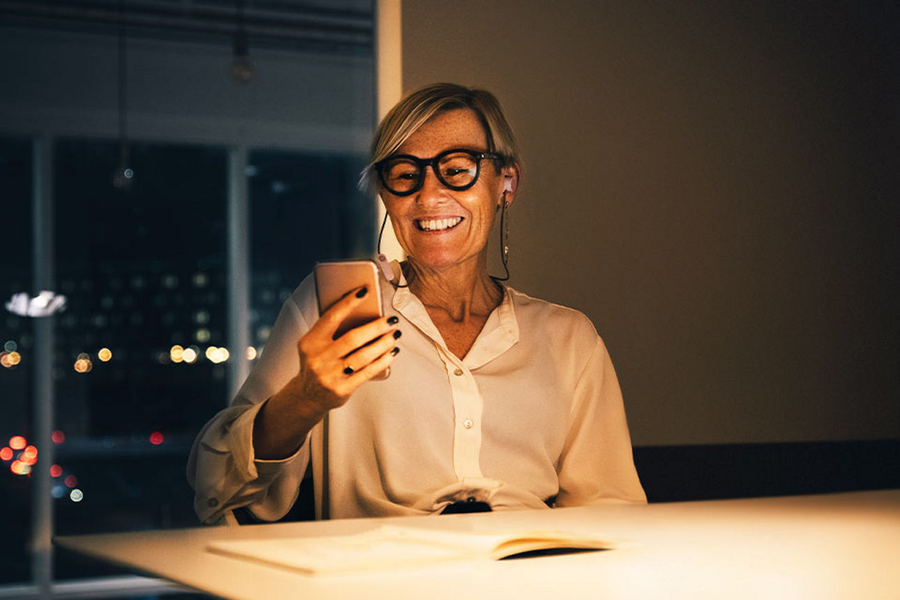 Eine Geschäftsfrau schaut lächelnd auf ihr Smartphone