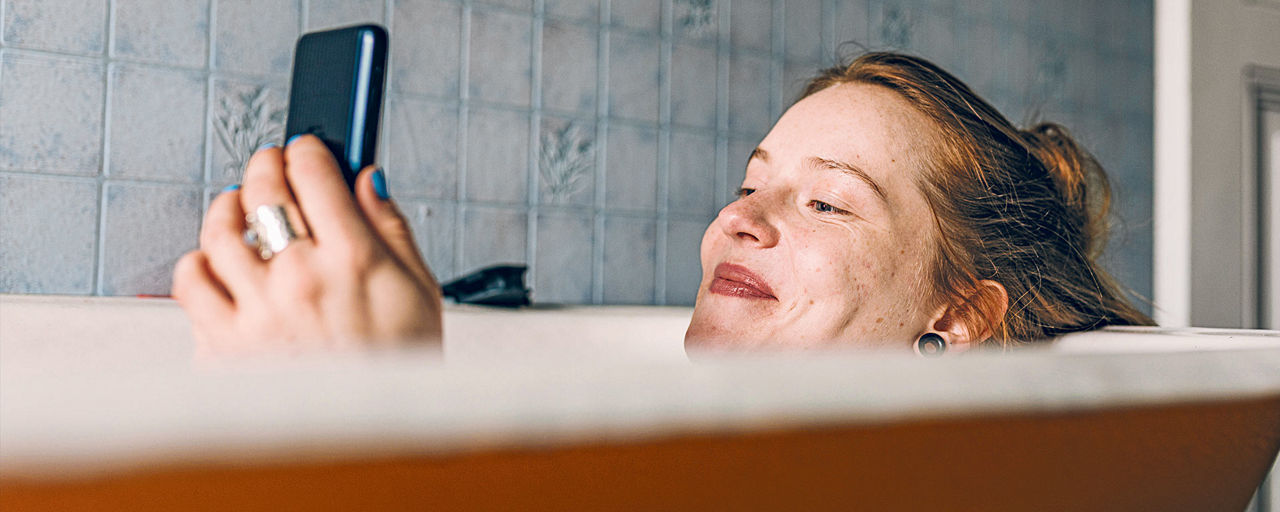 Eine Frau liegt in der Badewanne und schaut auf ihr Smartphone