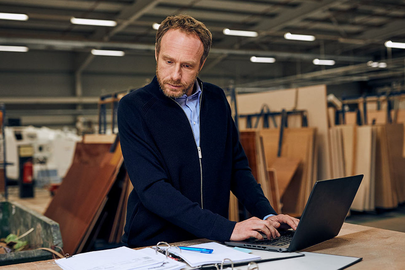 Mann schaut in Ordner, während er auf Laptop tippt