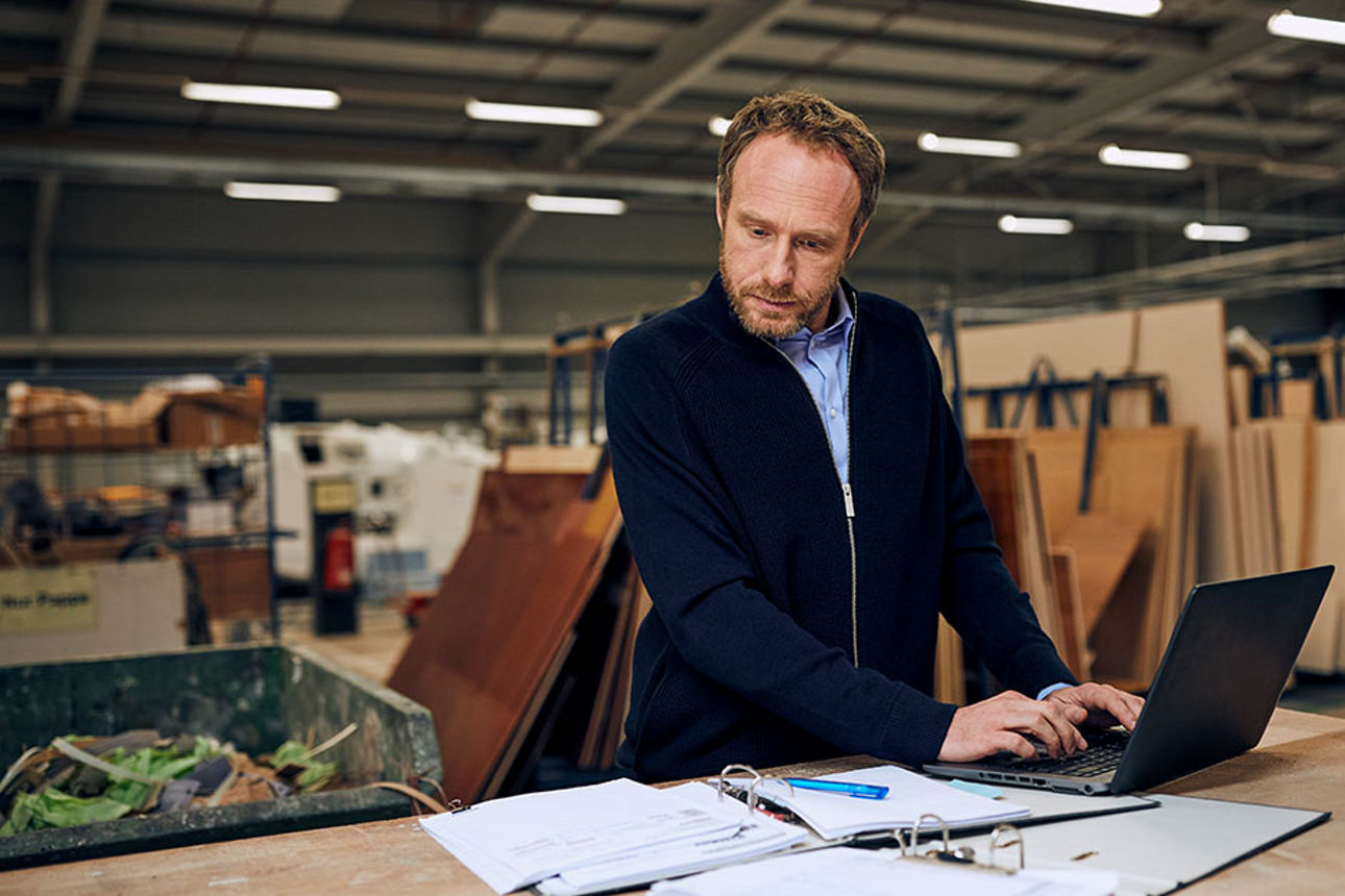 Ein Mann in einer Lagerhalle bei der Arbeit an einem Laptop.