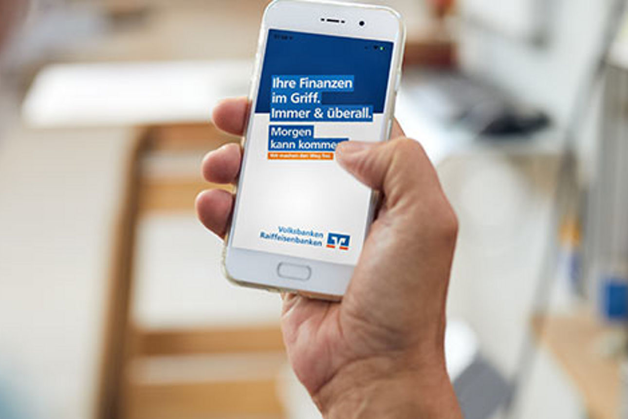 Eine Hand hält ein Smartphone mit geöffneter Volksbanken-Raiffeisenbanken-Seite