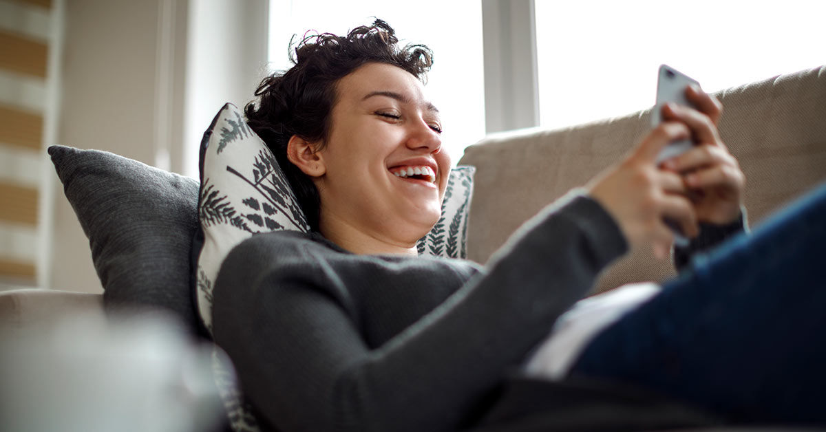 Junge Frauen am Handy liegend auf dem Sofa.