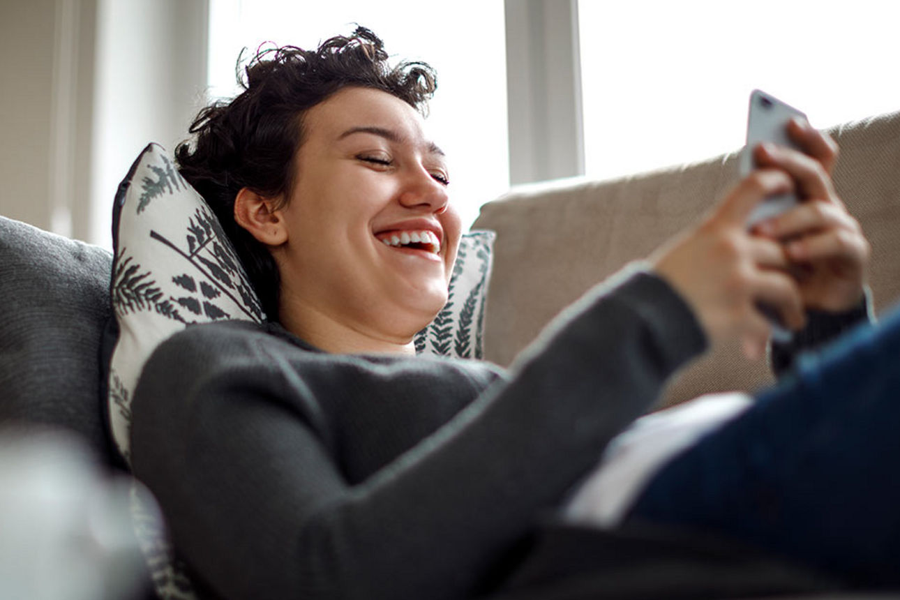 Junge Frauen am Handy liegend auf dem Sofa.
