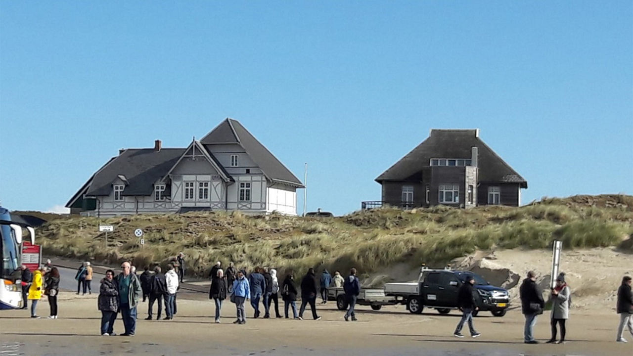 Strand mit Dünen, hinter denen sich typisch reetgedeckte Häuser in Dänemark erstrecken