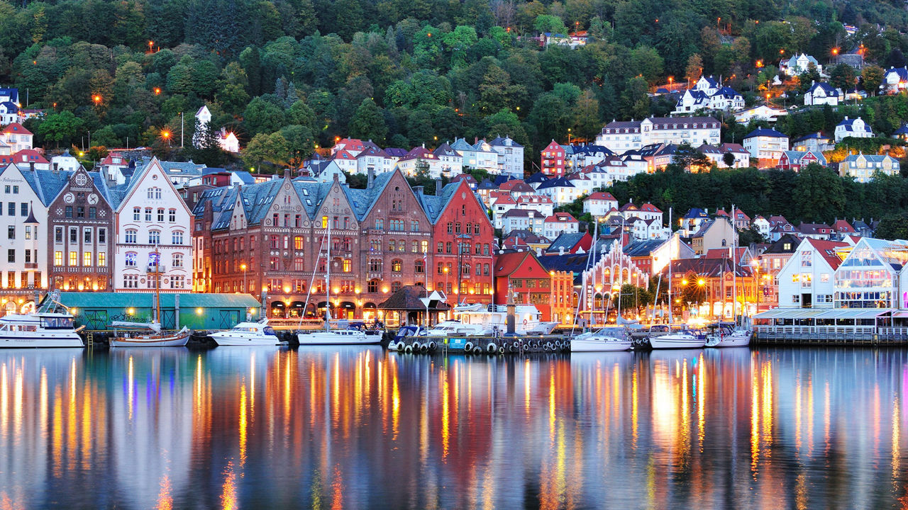 Skyline von Bergen in der Abenddämmerung. Die Lichter der Häuser spiegeln sich im Wasser.