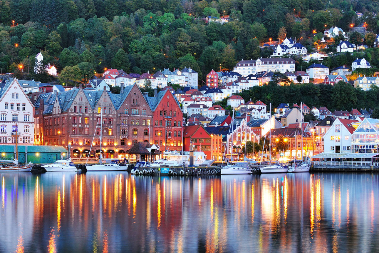 Skyline von Bergen in der Abenddämmerung. Die Lichter der Häuser spiegeln sich im Wasser.