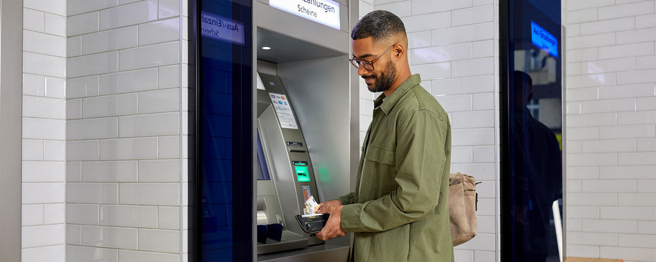 Mann steht am Geldautomaten und steckt Bargeld in sein Portemonnaie.