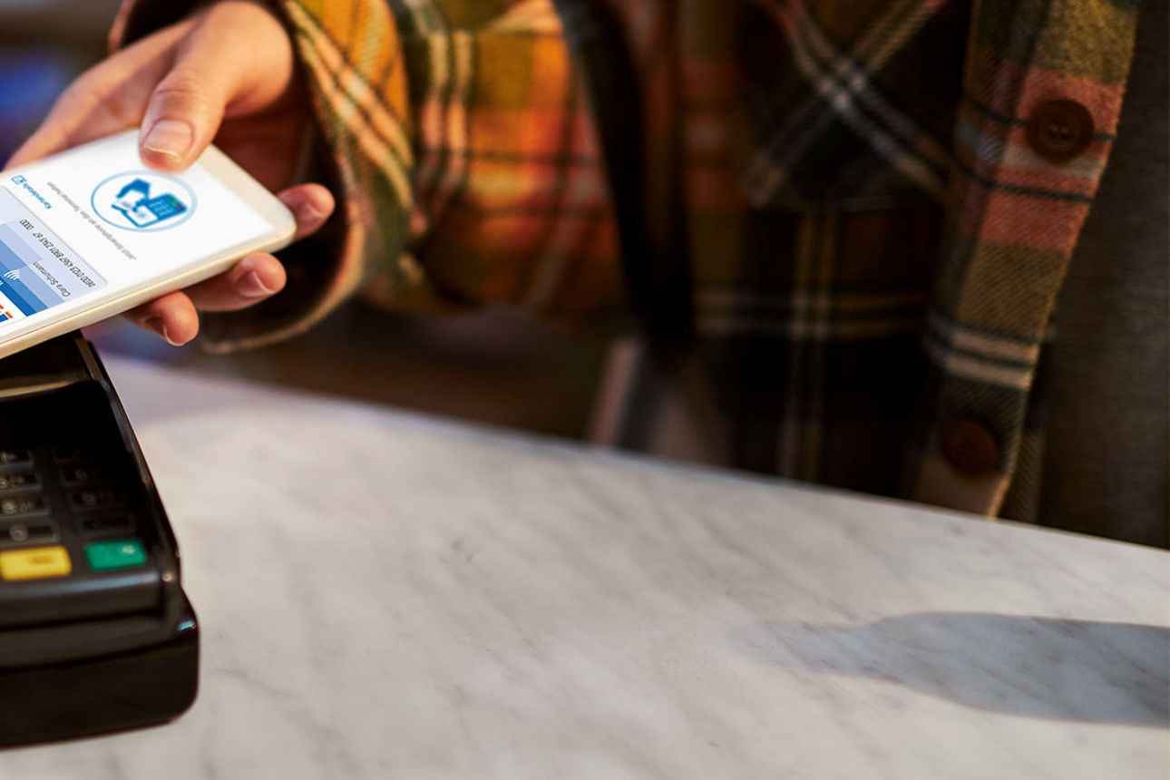 Ein Smartphone wird an ein Zahlungsterminal dran gehalten, um zu bezahlen.